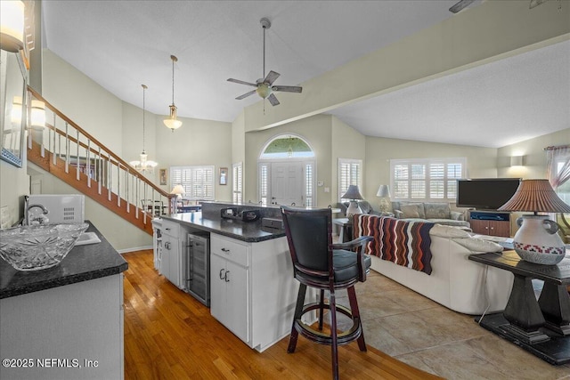 kitchen with lofted ceiling, hanging light fixtures, wine cooler, white cabinets, and a kitchen island