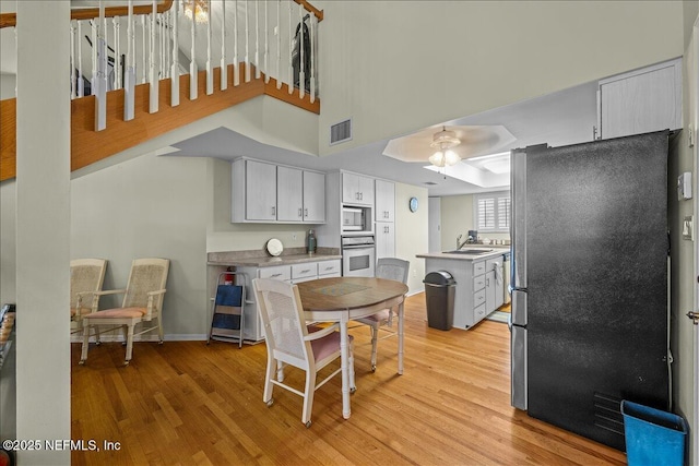 kitchen with sink, white cabinetry, stainless steel appliances, light hardwood / wood-style floors, and a high ceiling