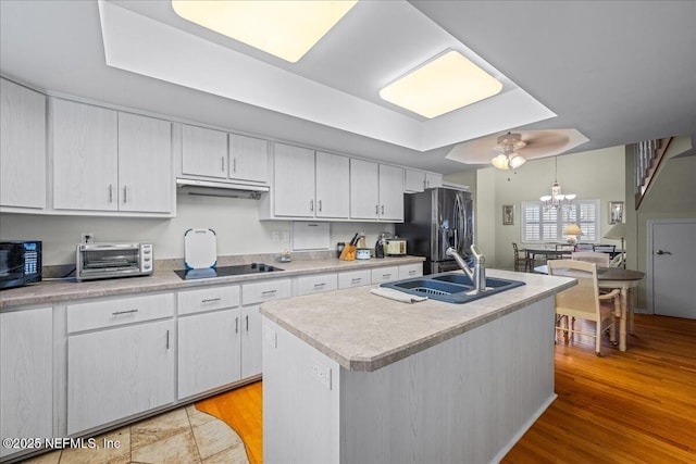 kitchen featuring sink, black appliances, an island with sink, pendant lighting, and white cabinets