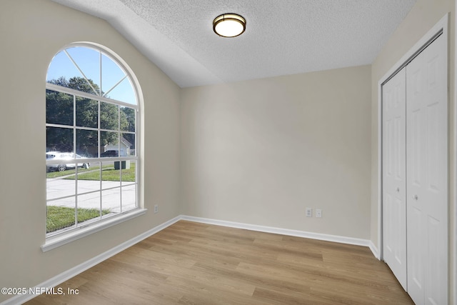 interior space with a textured ceiling, light wood-type flooring, lofted ceiling, and a healthy amount of sunlight