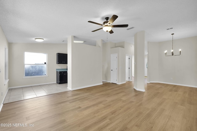 unfurnished living room with ceiling fan with notable chandelier, a textured ceiling, and light wood-type flooring