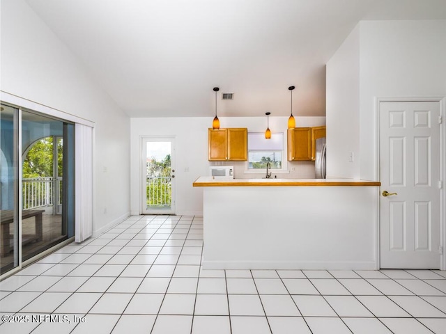 kitchen featuring hanging light fixtures, light tile patterned floors, kitchen peninsula, vaulted ceiling, and stainless steel fridge