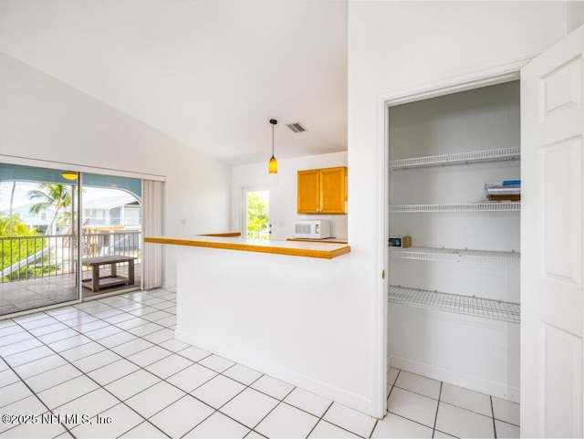 kitchen featuring pendant lighting, vaulted ceiling, kitchen peninsula, and light tile patterned floors