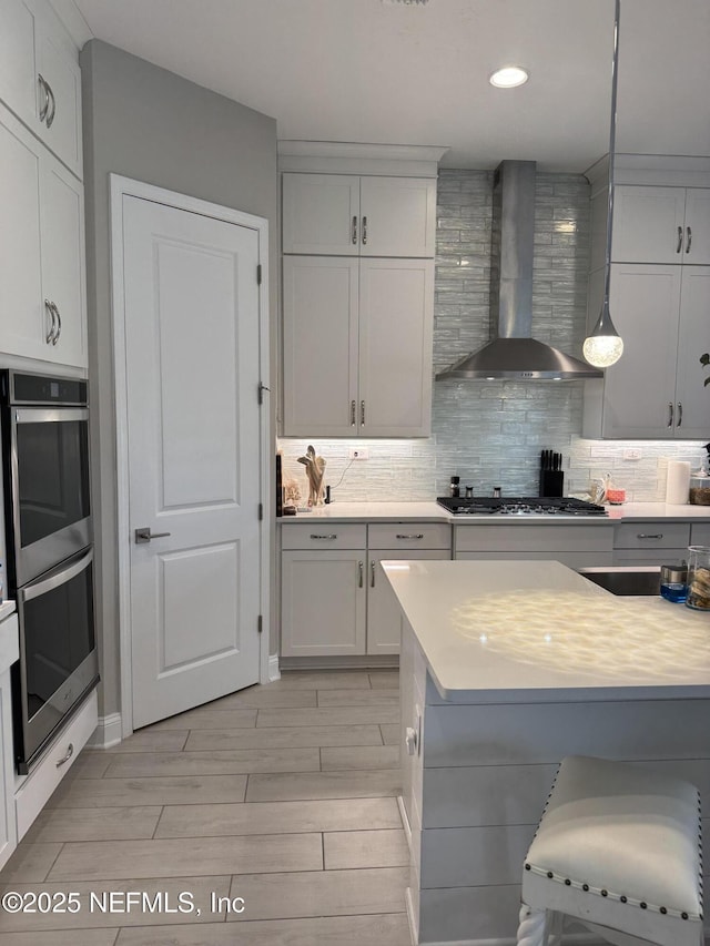 kitchen featuring pendant lighting, white cabinets, tasteful backsplash, wall chimney range hood, and stainless steel appliances