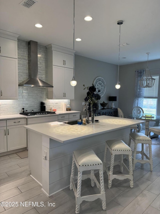 kitchen featuring sink, wall chimney range hood, white cabinets, and a kitchen island with sink