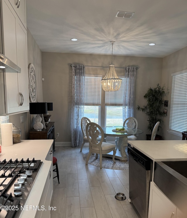 kitchen with a notable chandelier, dishwasher, white cabinetry, wall chimney range hood, and pendant lighting