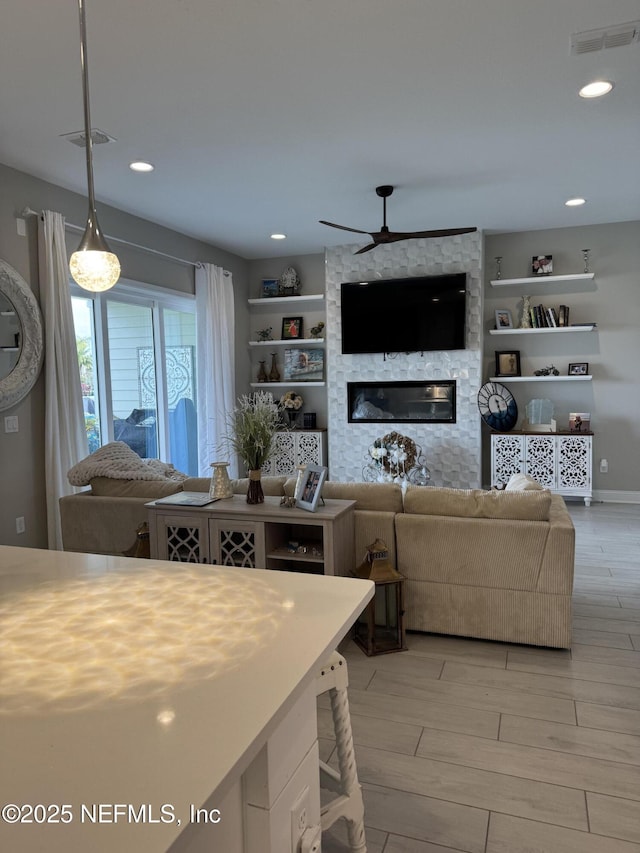 living room featuring light hardwood / wood-style floors, ceiling fan, built in features, and a stone fireplace