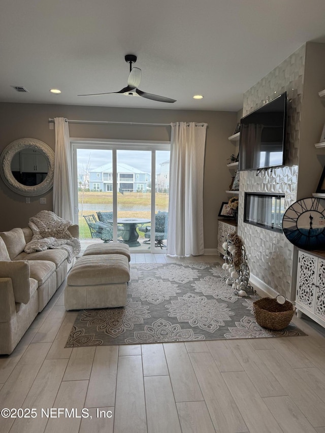 living room featuring ceiling fan and a stone fireplace