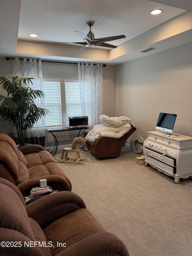 carpeted living room featuring ceiling fan and a tray ceiling