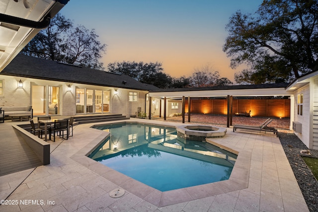 pool at dusk with an in ground hot tub and a patio