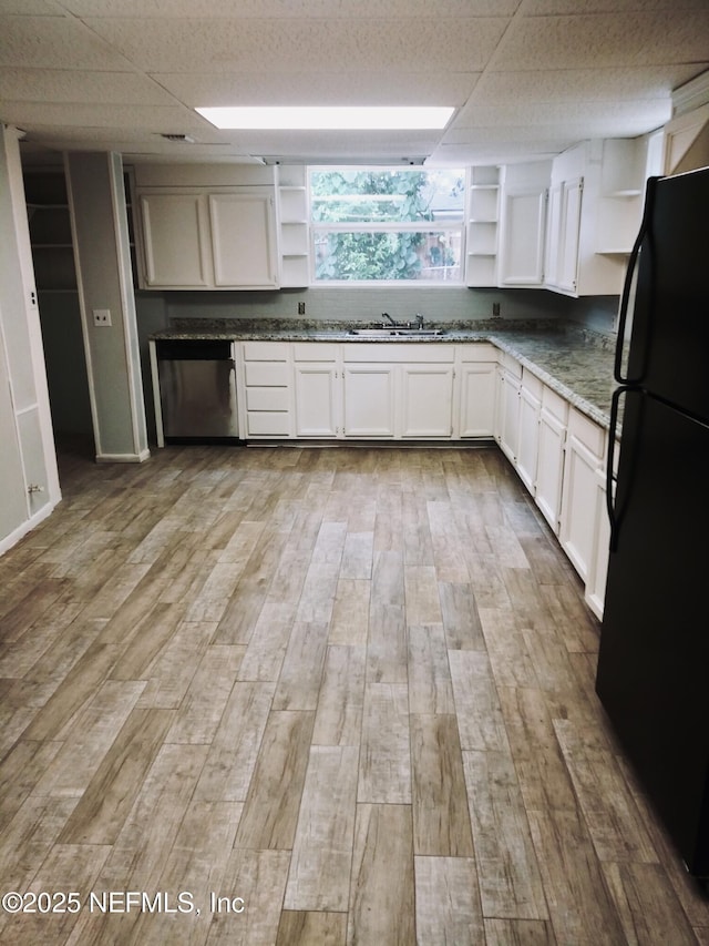 kitchen featuring light hardwood / wood-style floors, white cabinetry, a drop ceiling, dark stone countertops, and black fridge