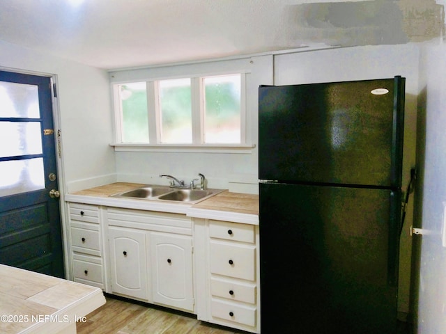 kitchen with sink, light hardwood / wood-style floors, black fridge, and white cabinetry