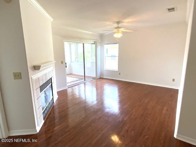 unfurnished living room with a tile fireplace, crown molding, dark hardwood / wood-style floors, and ceiling fan