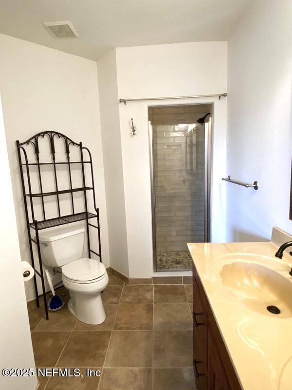 bathroom featuring tile patterned flooring, toilet, vanity, and walk in shower