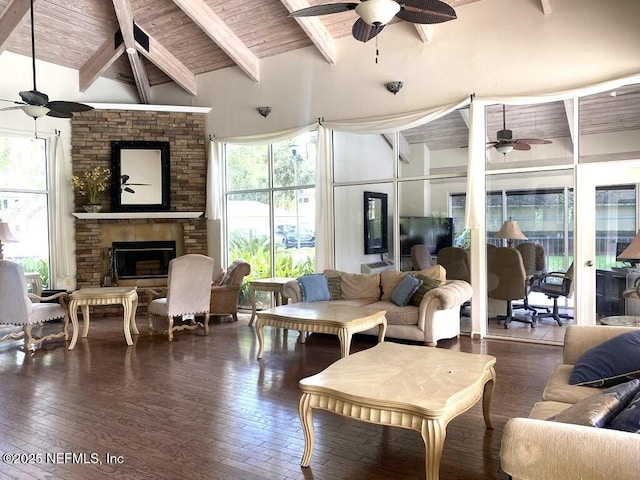 living room featuring a stone fireplace, high vaulted ceiling, ceiling fan, dark wood-type flooring, and beam ceiling