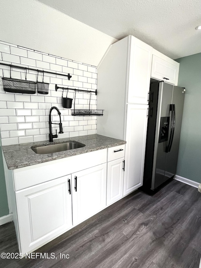 kitchen with a textured ceiling, white cabinetry, stainless steel refrigerator with ice dispenser, sink, and vaulted ceiling