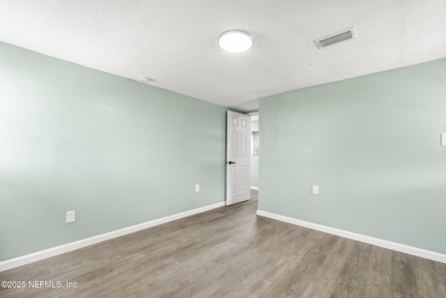 unfurnished room featuring visible vents, a textured ceiling, baseboards, and wood finished floors