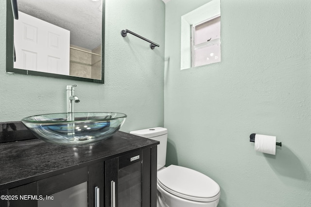 bathroom featuring toilet, a textured wall, and vanity