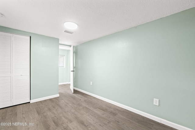 unfurnished bedroom featuring a closet, visible vents, a textured ceiling, light wood-type flooring, and baseboards