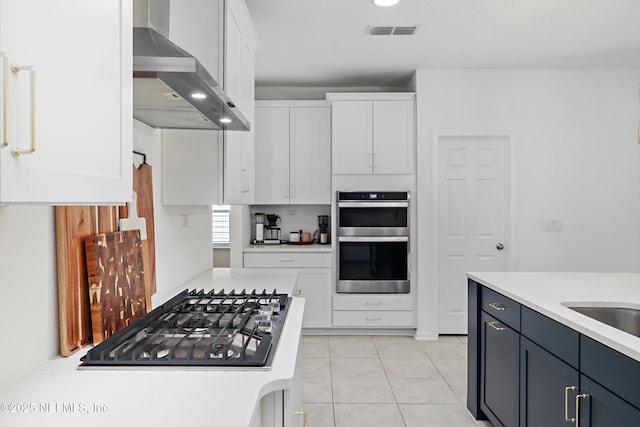 kitchen featuring visible vents, light countertops, appliances with stainless steel finishes, white cabinetry, and wall chimney range hood