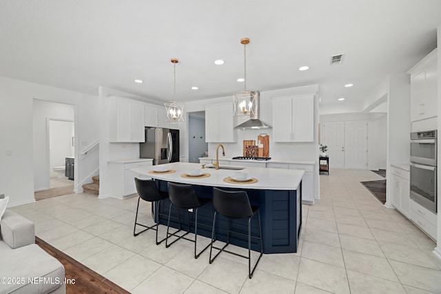 kitchen with a center island with sink, a sink, stainless steel appliances, wall chimney exhaust hood, and light countertops