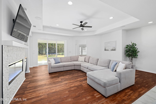 living area featuring a stone fireplace, recessed lighting, a raised ceiling, and wood finished floors