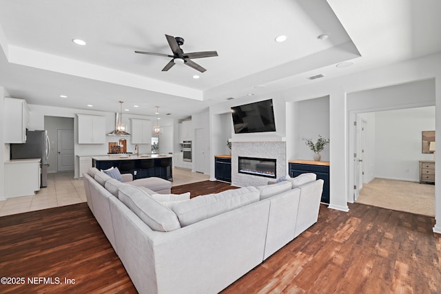 living room featuring recessed lighting, a tray ceiling, a glass covered fireplace, and light wood finished floors