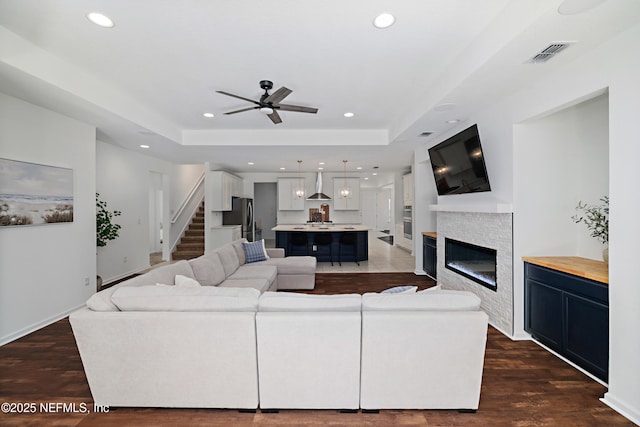 living room with visible vents, stairway, a tray ceiling, recessed lighting, and a glass covered fireplace