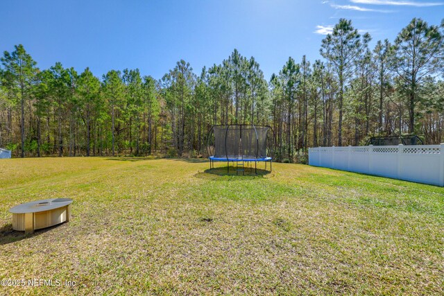 view of yard featuring a trampoline, a wooded view, and fence