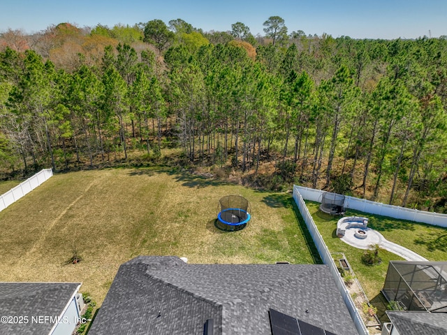 view of yard featuring a trampoline, a fenced backyard, a forest view, and an outdoor fire pit