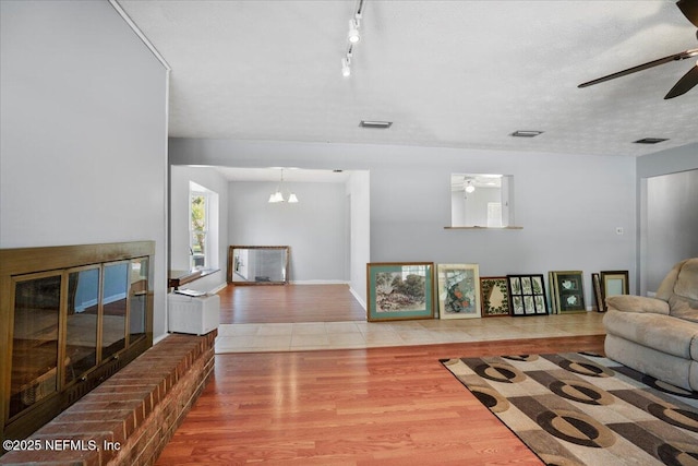 living room featuring a textured ceiling, hardwood / wood-style flooring, ceiling fan with notable chandelier, and a brick fireplace