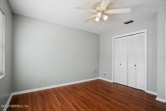 unfurnished bedroom with ceiling fan, dark wood-type flooring, a textured ceiling, and a closet