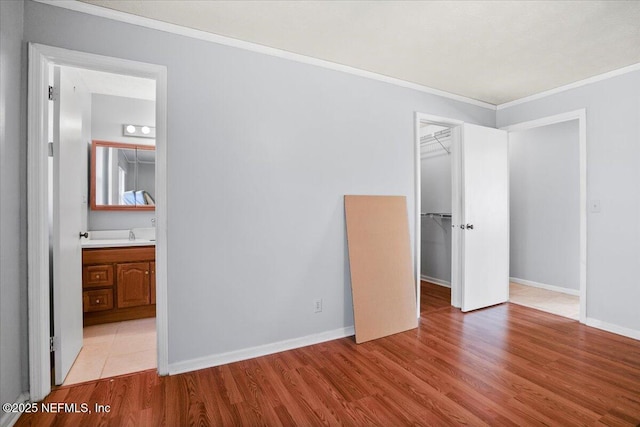 unfurnished bedroom with ensuite bathroom, crown molding, a walk in closet, a closet, and light hardwood / wood-style flooring