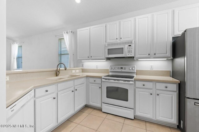 kitchen with sink, white appliances, light tile patterned floors, and white cabinets