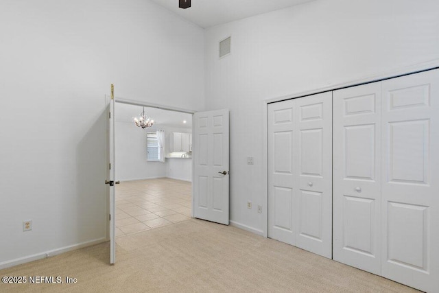 unfurnished bedroom featuring a towering ceiling, light colored carpet, an inviting chandelier, and a closet