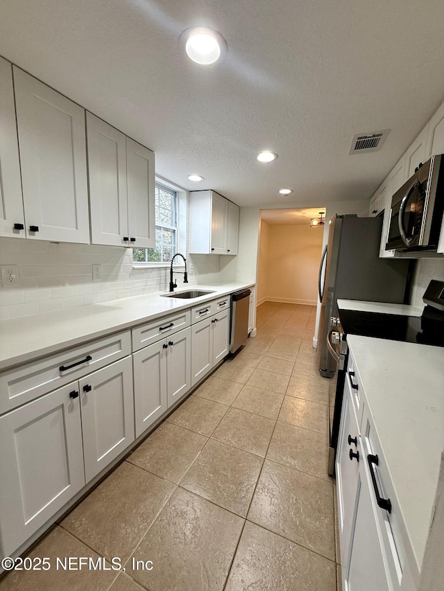 kitchen featuring sink, white cabinets, decorative backsplash, stainless steel appliances, and a textured ceiling