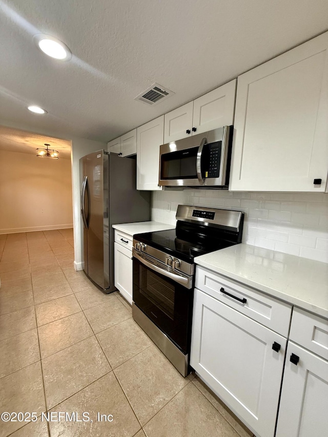 kitchen with light tile patterned floors, white cabinetry, stainless steel appliances, a textured ceiling, and decorative backsplash