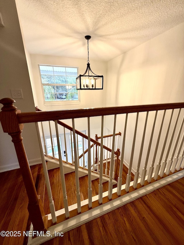 stairway with hardwood / wood-style floors, a textured ceiling, and an inviting chandelier