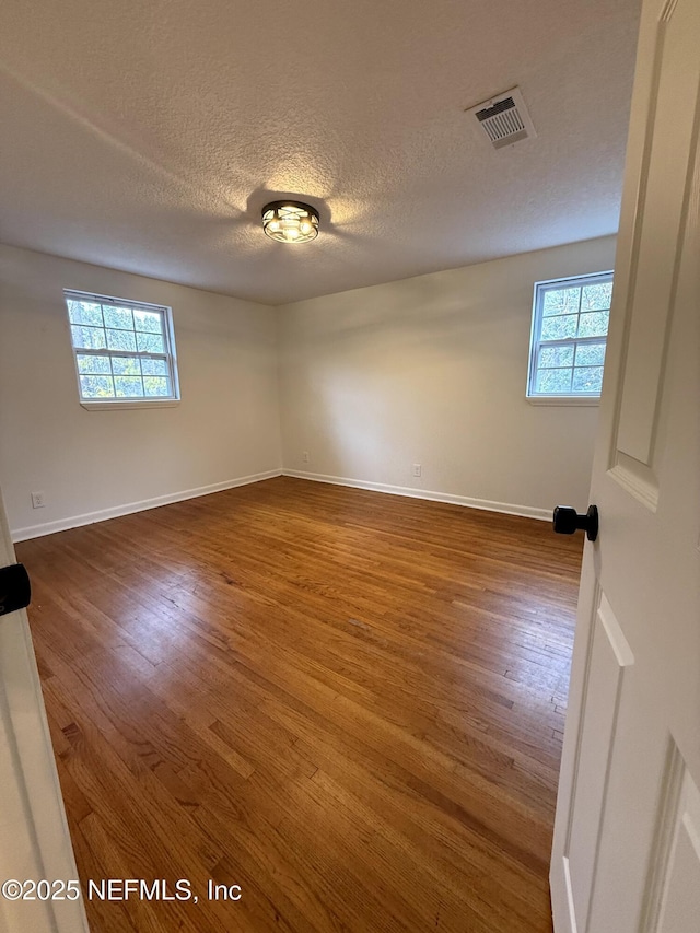 empty room featuring a wealth of natural light, hardwood / wood-style floors, and a textured ceiling