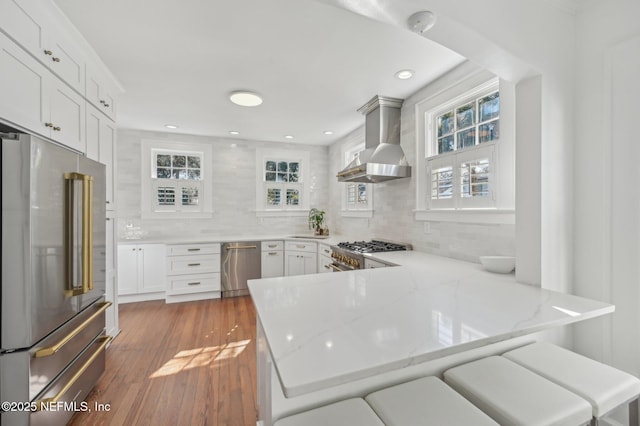 kitchen with wall chimney range hood, white cabinets, kitchen peninsula, and high quality appliances