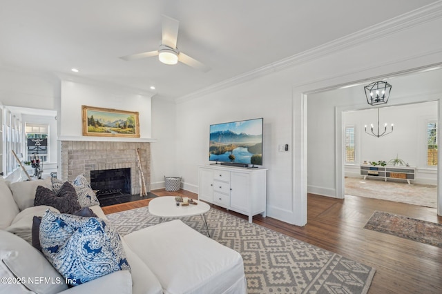 living room featuring hardwood / wood-style flooring, crown molding, ceiling fan with notable chandelier, and a fireplace