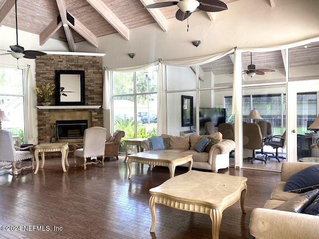 living room featuring dark wood-type flooring, ceiling fan, high vaulted ceiling, a stone fireplace, and beamed ceiling