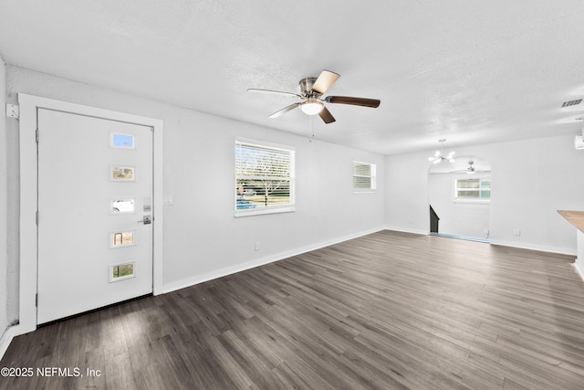 unfurnished living room featuring ceiling fan with notable chandelier, plenty of natural light, and dark hardwood / wood-style floors