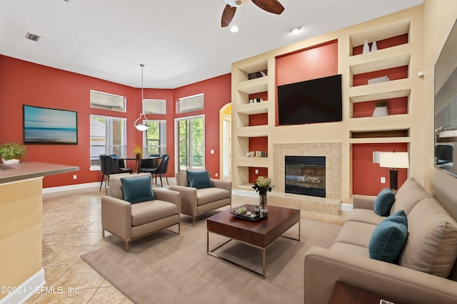 tiled living room featuring ceiling fan, built in shelves, and a tile fireplace