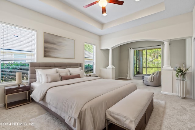 bedroom with ceiling fan, light carpet, a tray ceiling, and ornate columns