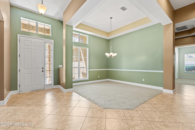 tiled foyer entrance featuring a raised ceiling and a notable chandelier