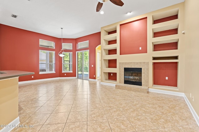 unfurnished living room with ceiling fan, built in shelves, a tiled fireplace, and tile patterned flooring