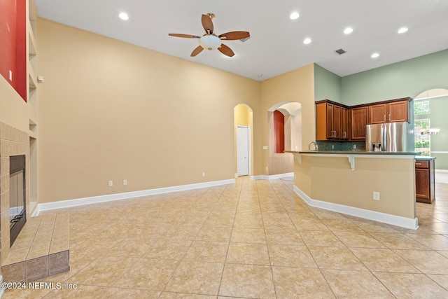 kitchen featuring a kitchen breakfast bar, stainless steel fridge, a tiled fireplace, backsplash, and light tile patterned floors