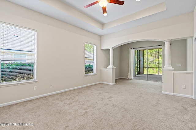 carpeted empty room featuring ceiling fan, decorative columns, and a tray ceiling