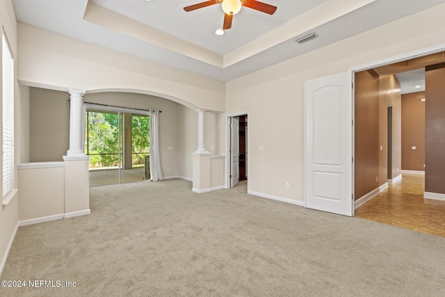 unfurnished room with decorative columns, light colored carpet, ceiling fan, and a raised ceiling